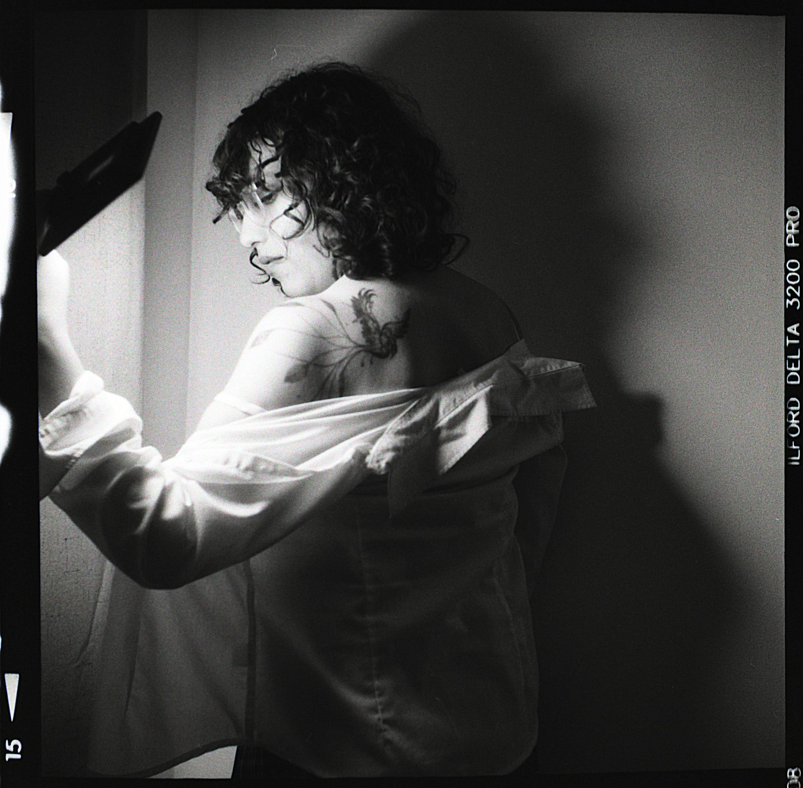 Shoulder turned, tattoo visible, light raking across the skin